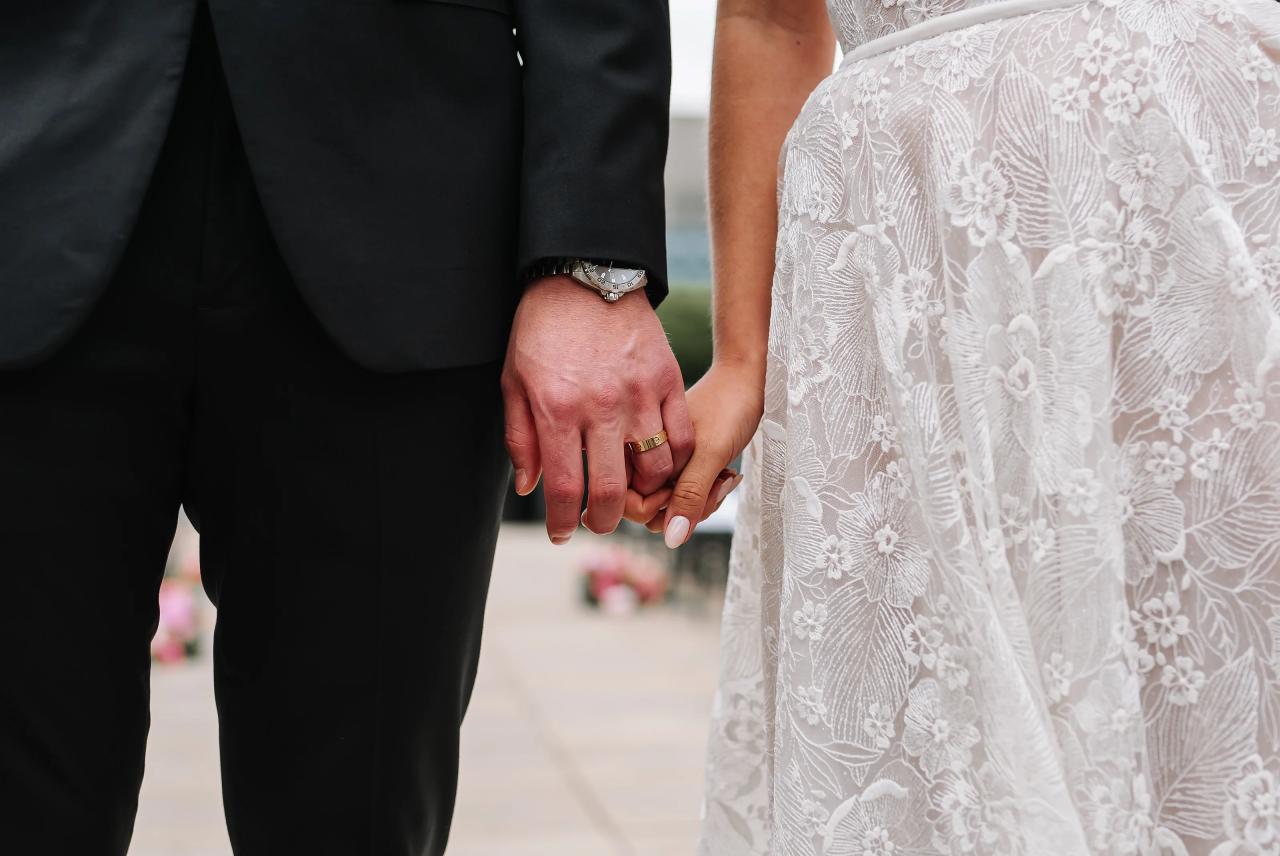 Close-up of a bride and groom’s hands holding during a wedding ceremony, with the bride’s lace dress details visible. Wedding photography at Tribeca Rooftop + 360°, New York, NY.