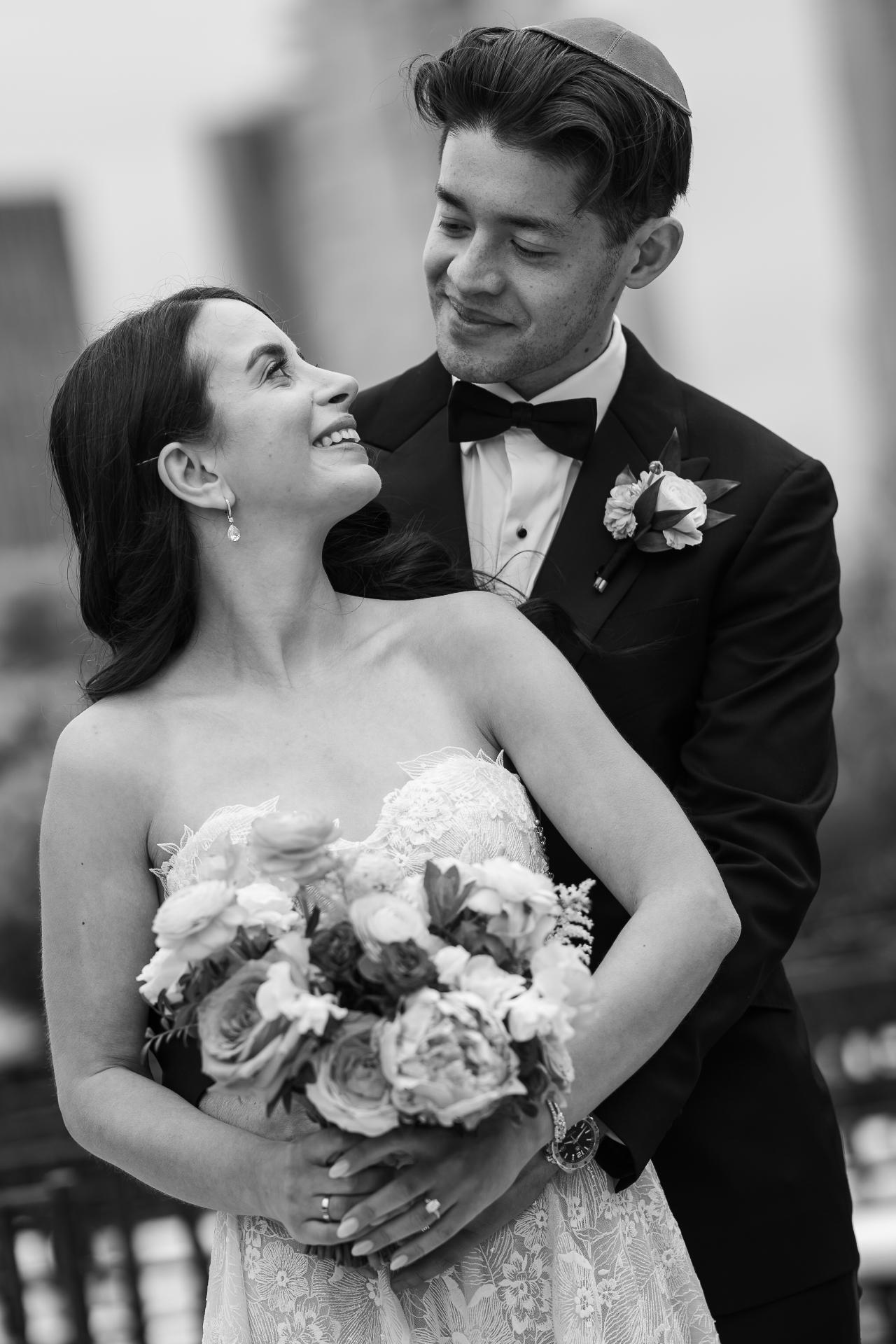 Black and white close-up of a bride and groom embracing, smiling at each other as they hold a bouquet. Wedding photography at Tribeca Rooftop + 360°, New York, NY.