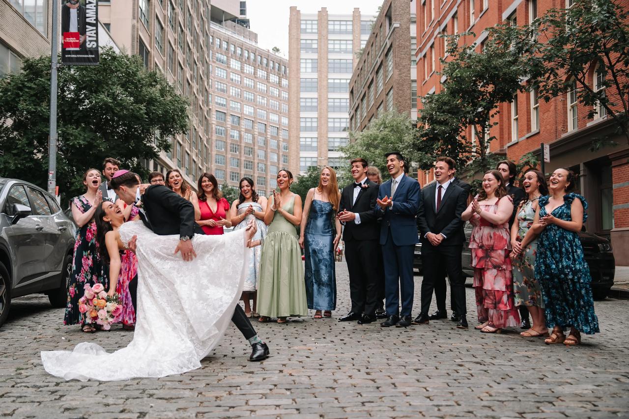 Bride and groom being lifted in celebration as a group of guests clap and cheer outdoors on a city street. Wedding photography at Tribeca Rooftop + 360°, New York, NY.