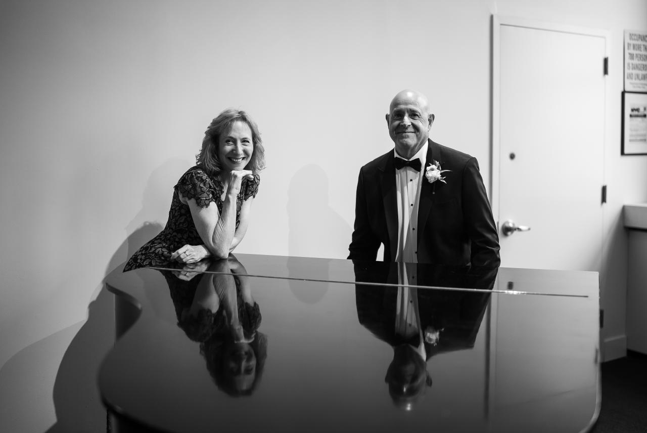 Black-and-white wedding portrait of a smiling bride and groom reflected in a glossy surface, posed in a bright hallway. Wedding photography at Tribeca Rooftop + 360°, New York, NY.
