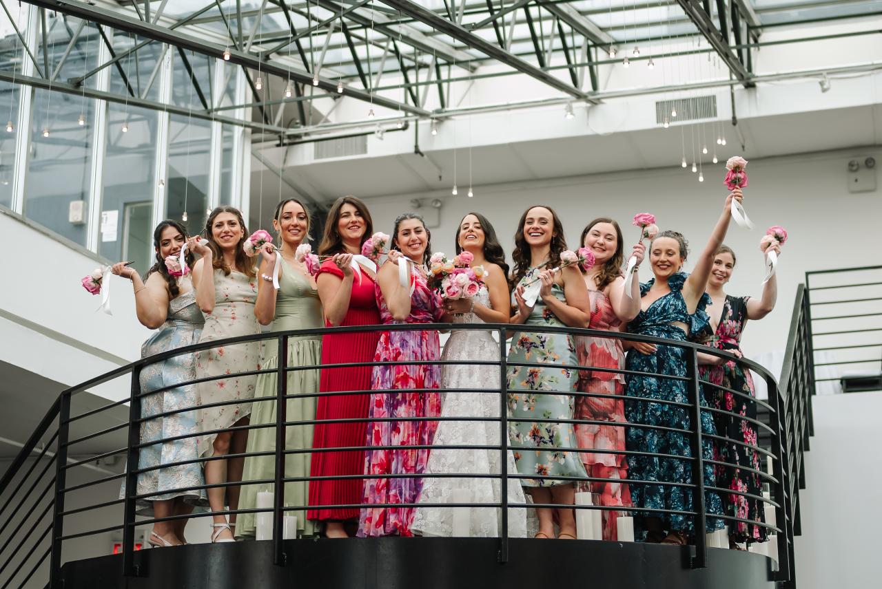 Wedding guests on a curved indoor balcony cheering and holding pink bouquets above the railing. Wedding photography at Tribeca Rooftop + 360°, New York, NY.
