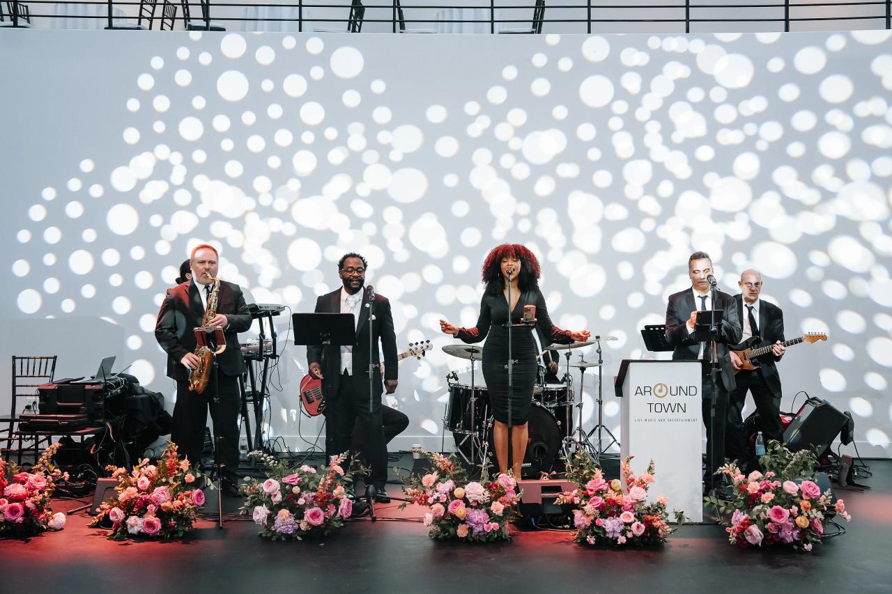Live band finale on a wedding stage with musicians singing and playing instruments in front of a sparkling dot light projection and floral arrangements. Wedding photography at Tribeca Rooftop + 360°, New York, NY.