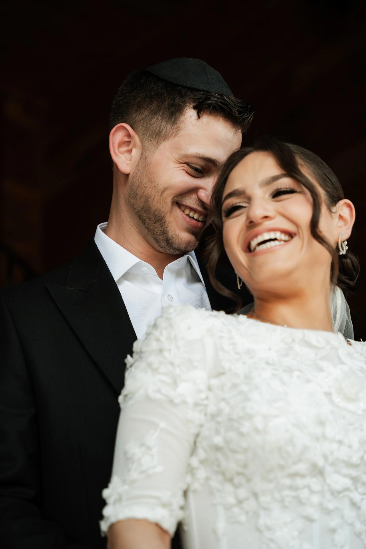 Smiling bride and groom in close embrace, laughing together against a dark background at their wedding portrait. Wedding photography at The Barn At Indian Ridge, Highland, NY.