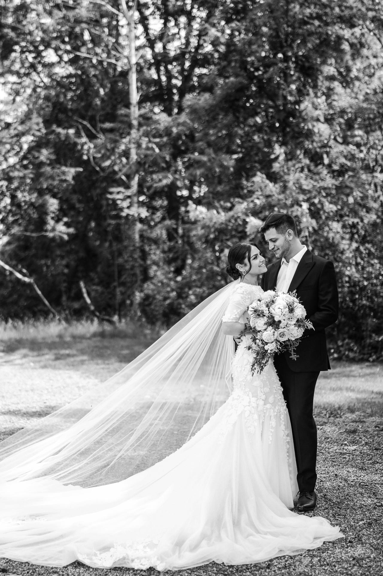 Black-and-white wedding portrait of a bride and groom outdoors, standing close with a flowing veil and bouquet in the garden. Wedding photography at The Barn At Indian Ridge, Highland, NY.
