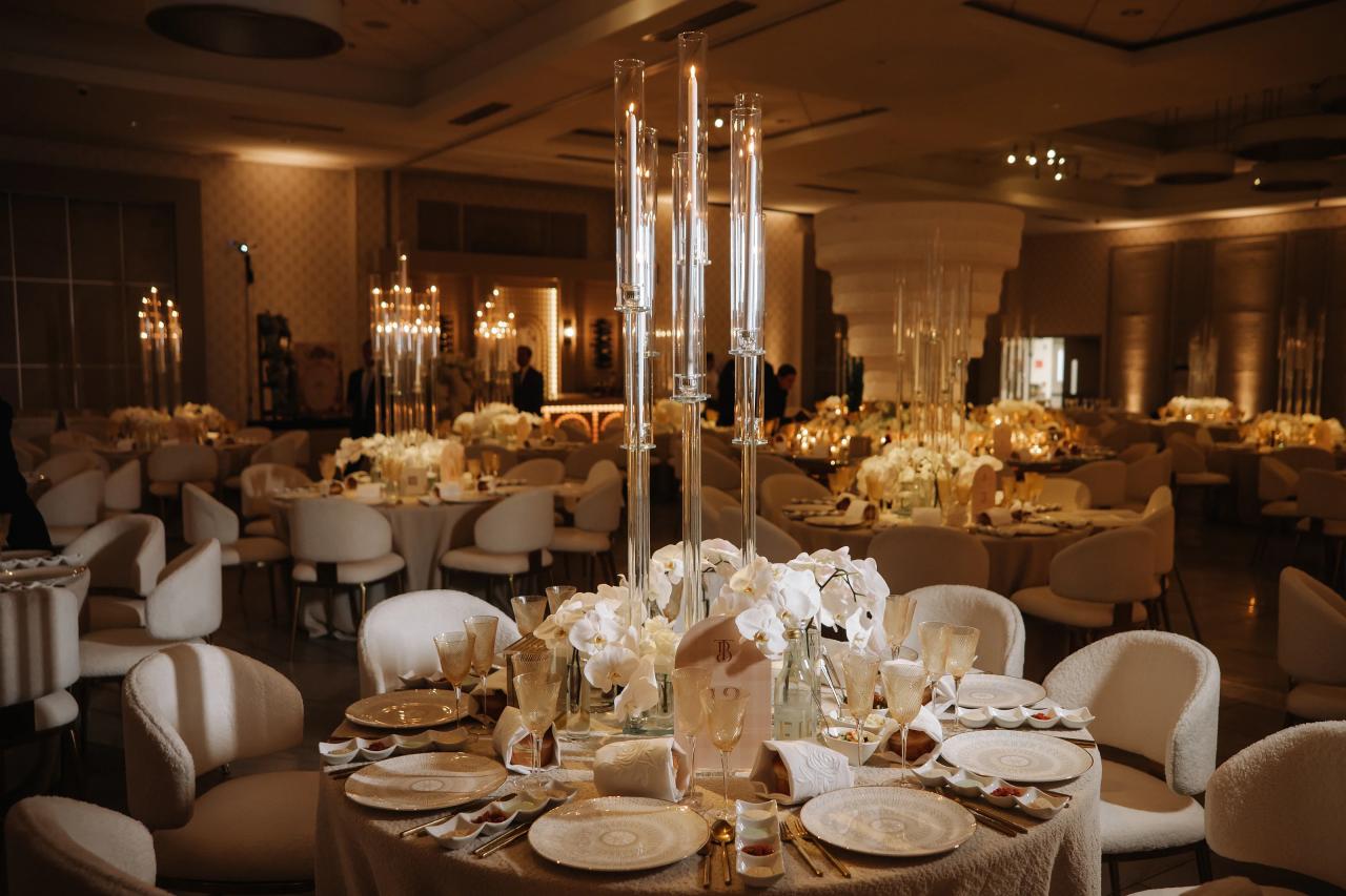 Warmly lit bar mitzvah tablescape with white orchids, tall glass candle centerpieces, place settings and glassware. Bar Mitzvah photography at Hilton Garden Inn Springfield, Springfield, NJ.