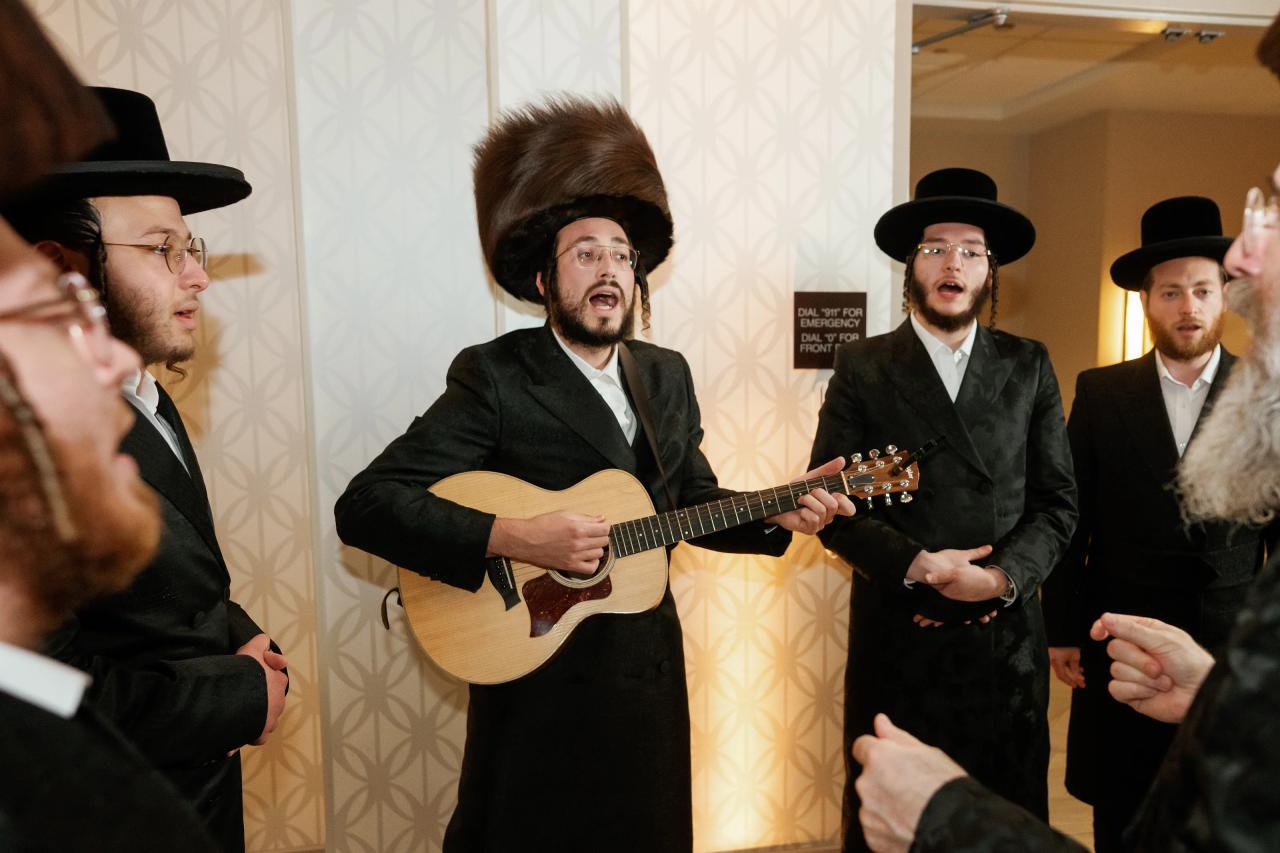 Indoor simcha band performance with a guitarist at center singing and playing, guests reacting at the sides. Bar Mitzvah photography at Hilton Garden Inn Springfield, Springfield, NJ.