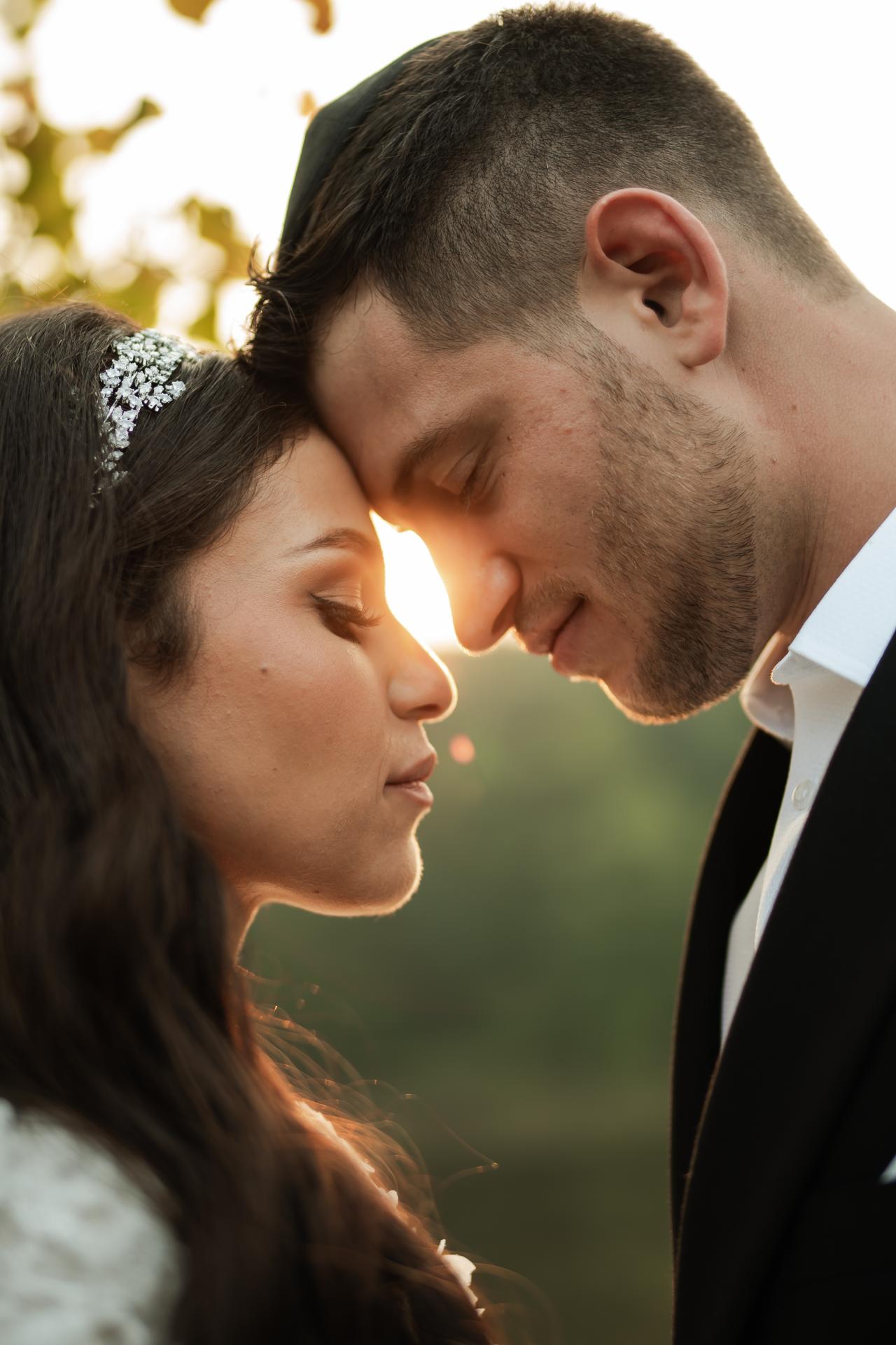 Bride and groom sharing an intimate close moment with foreheads touching in warm golden-hour light outdoors. Wedding photography at The Barn At Indian Ridge, Highland, NY.