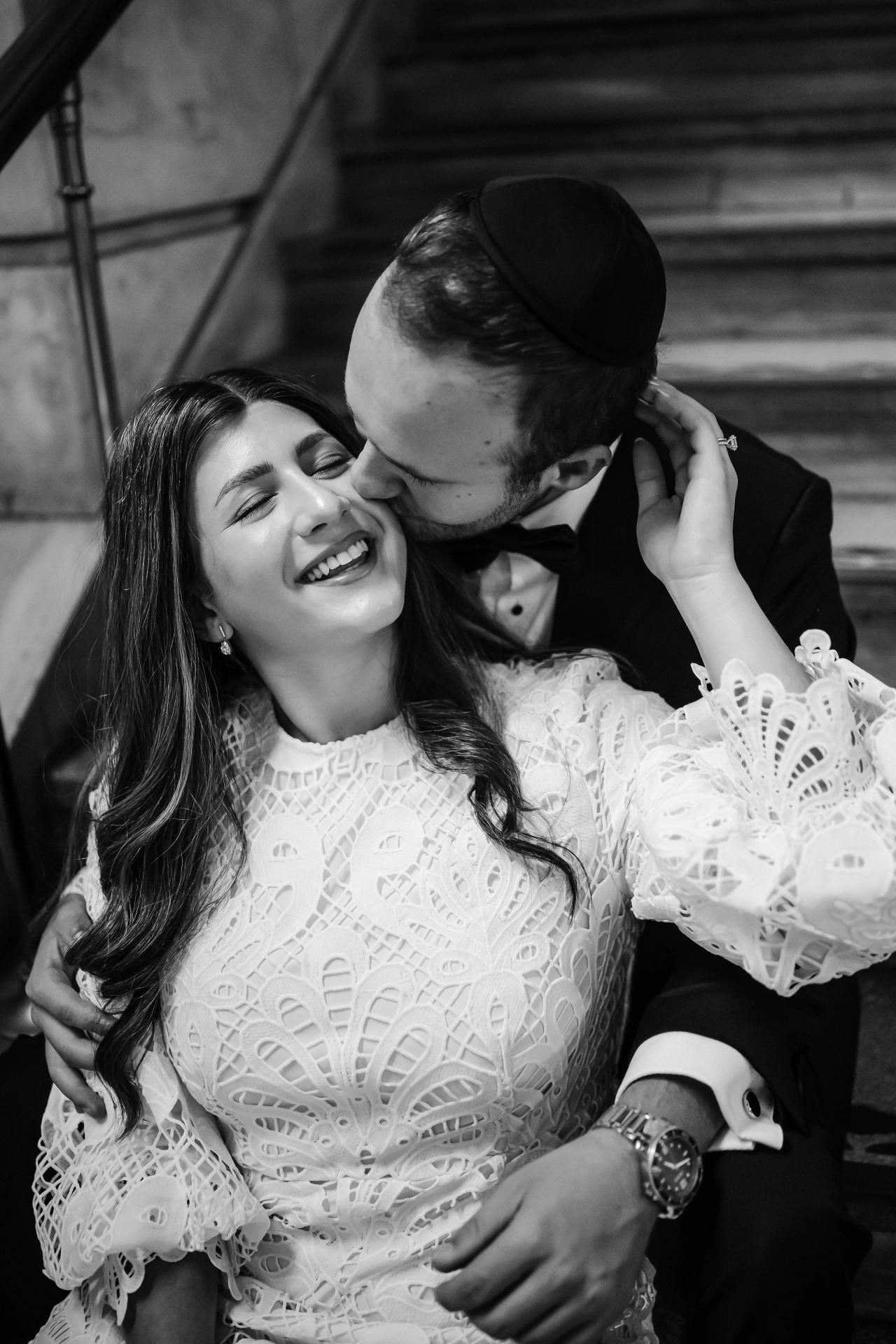 Black-and-white intimate close-up of a bride and groom embracing, smiling and leaning into each other during the celebration.
