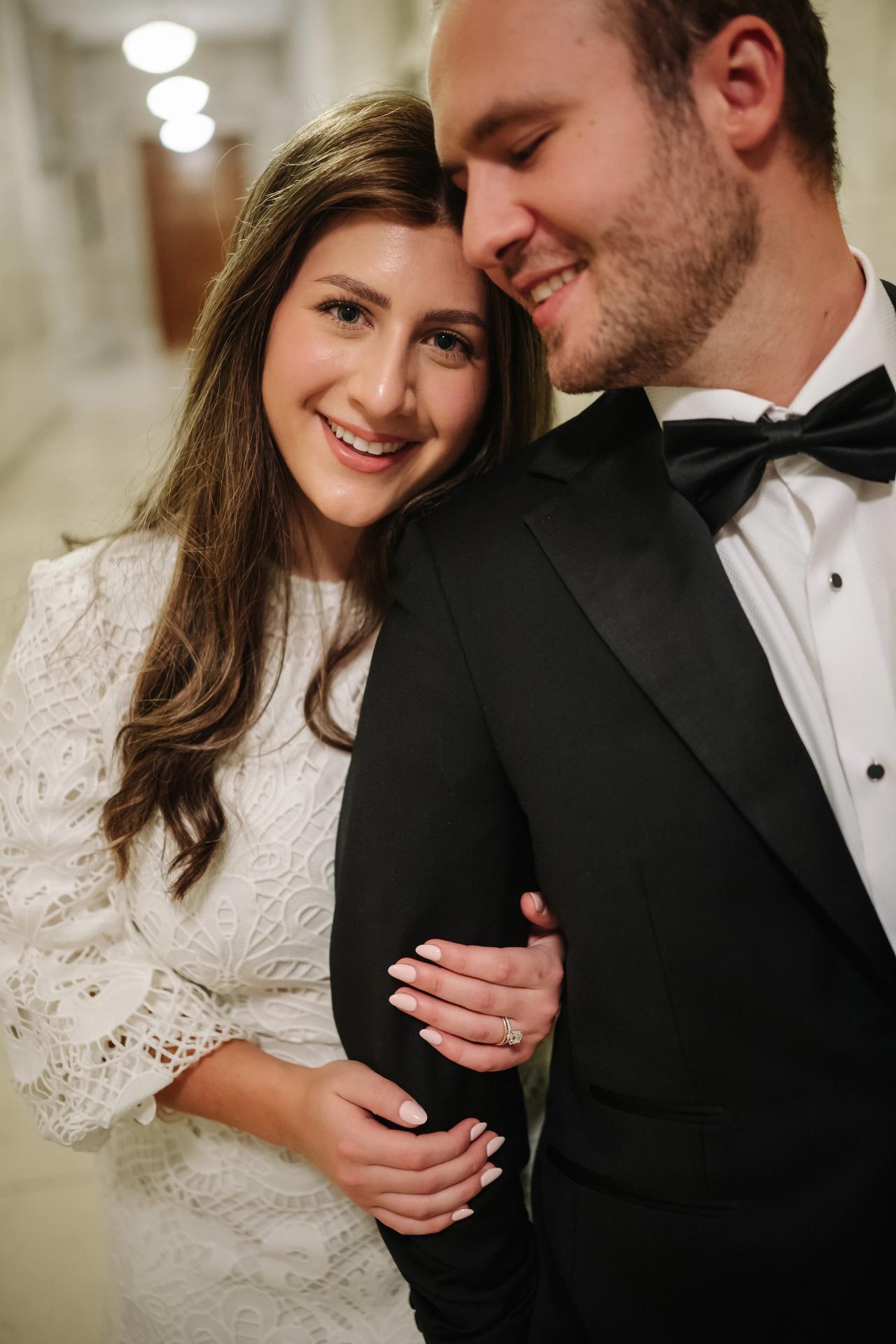 Close, warm-lit portrait of a bride and groom embracing and smiling in an indoor venue.