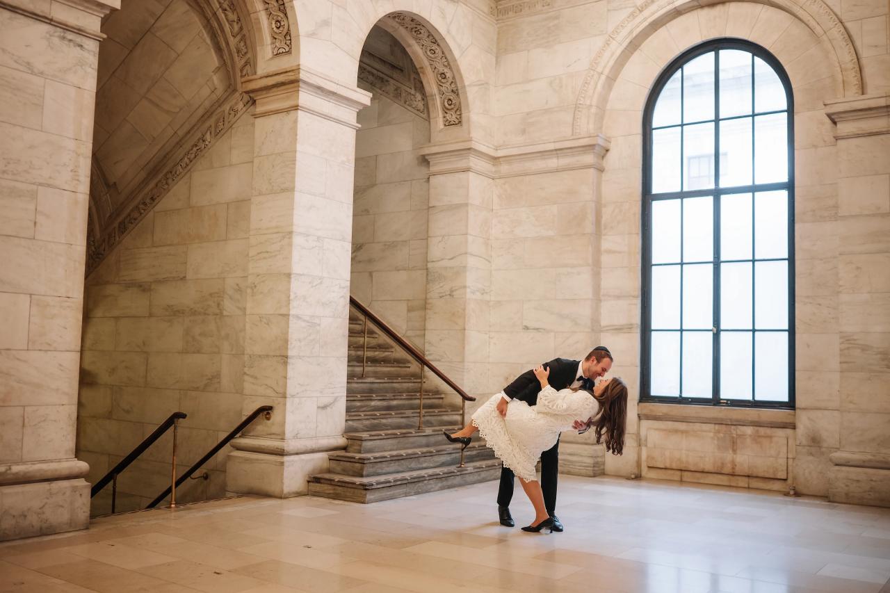 Wedding couple in a close embrace posing in a grand marble hall, backlit by bright window light.