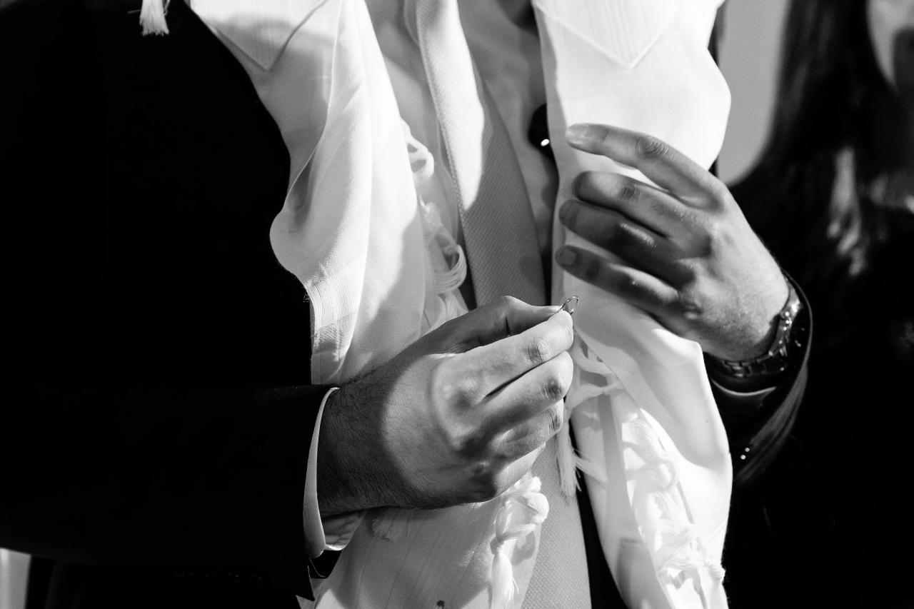 Black-and-white close-up of hands adjusting a bride’s white dress fabric and veil near the waist, with dramatic contrast and texture. Wedding photography at Bellworks, Holmdel, NJ.