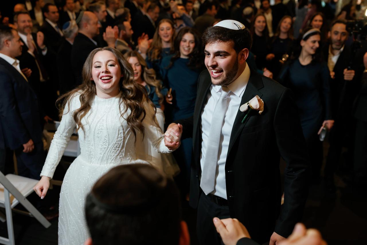 Laughing bride and groom in front of a crowded dance floor at a formal reception, warm indoor lighting, shallow depth of field. Wedding photography at Bellworks, Holmdel, NJ.