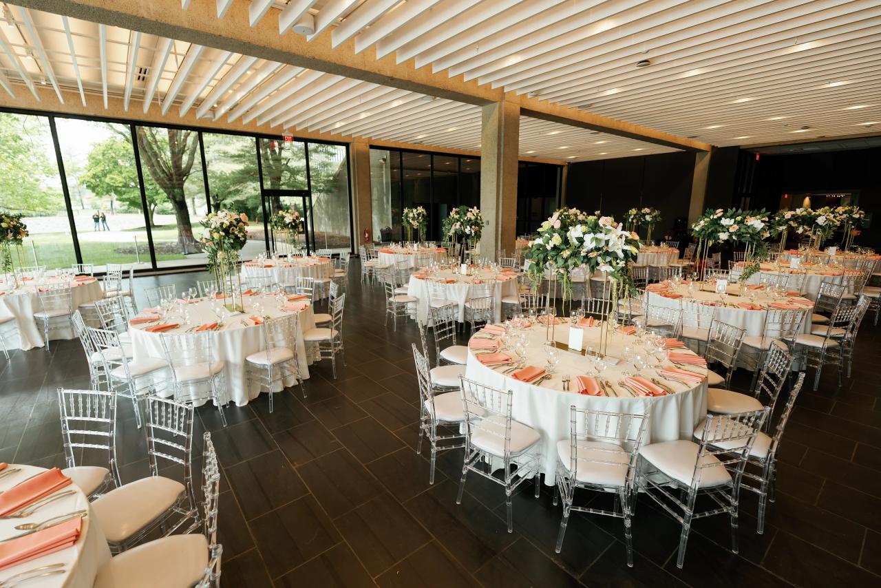 Reception banquet tables with white linens, silver chairs, and pastel floral centerpieces in a bright event hall. Wedding photography at Bellworks, Holmdel, NJ.