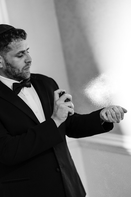 Black-and-white portrait of a bearded man in a tuxedo adjusting his sleeve, with soft directional light and fine particles floating in the background.