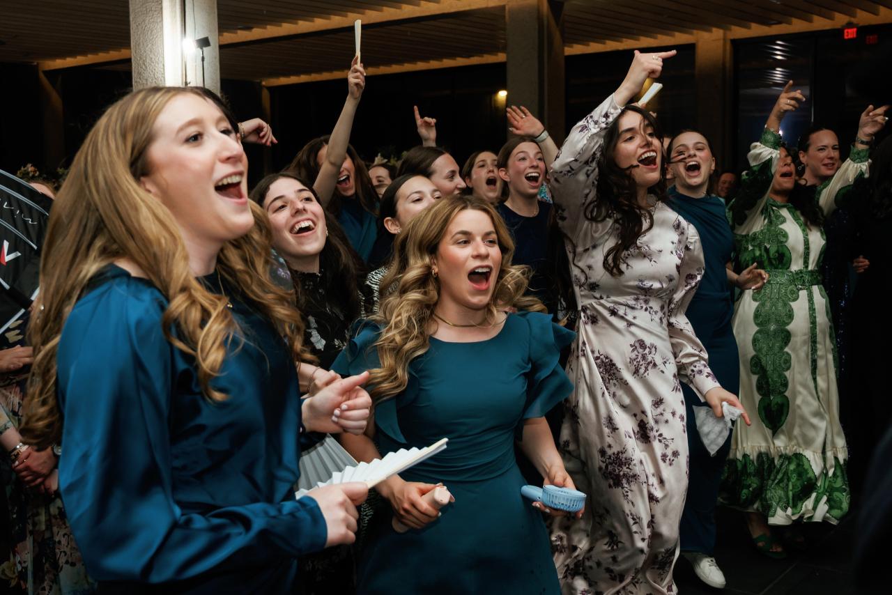 A lively crowd of women cheering and dancing at a reception, with multiple guests laughing, shouting, and raising their hands in celebration. Wedding photography at Bellworks, Holmdel, NJ.