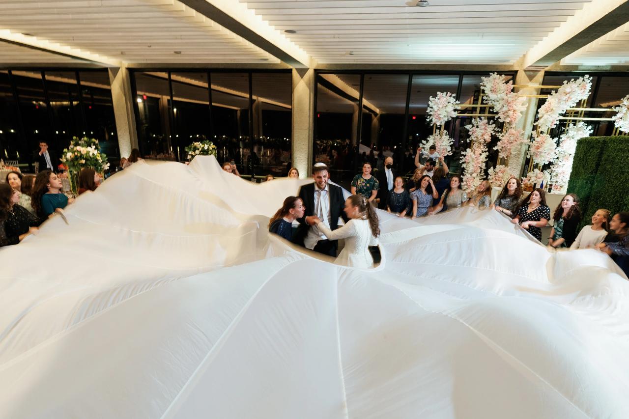 Couple dancing through flowing white fabric at a wedding reception, surrounded by guests and floral décor in an evening indoor setting. Wedding photography at Bellworks, Holmdel, NJ.