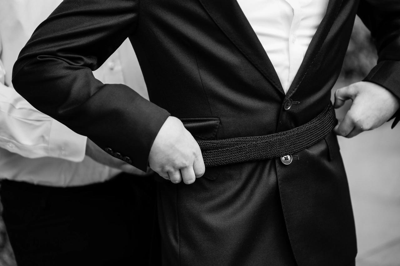 Black-and-white close-up of the Bar Mitzvah boy’s hands adjusting his belt. Bar Mitzvah photography at The Arches, Brooklyn, NY.