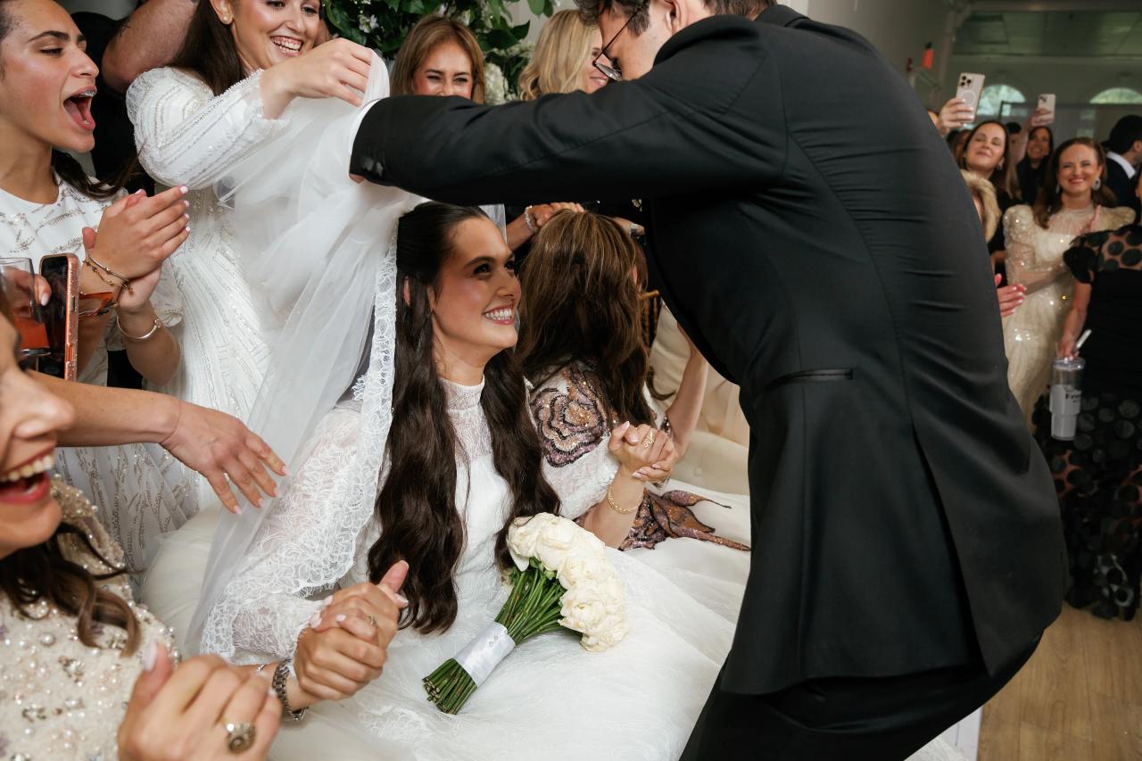 The bride in a white veil laughs with the groom as guests cheer around them during a fast-moving dance moment at a wedding. Wedding photography at Falkirk Estate Country Club, Central Valley, NY.