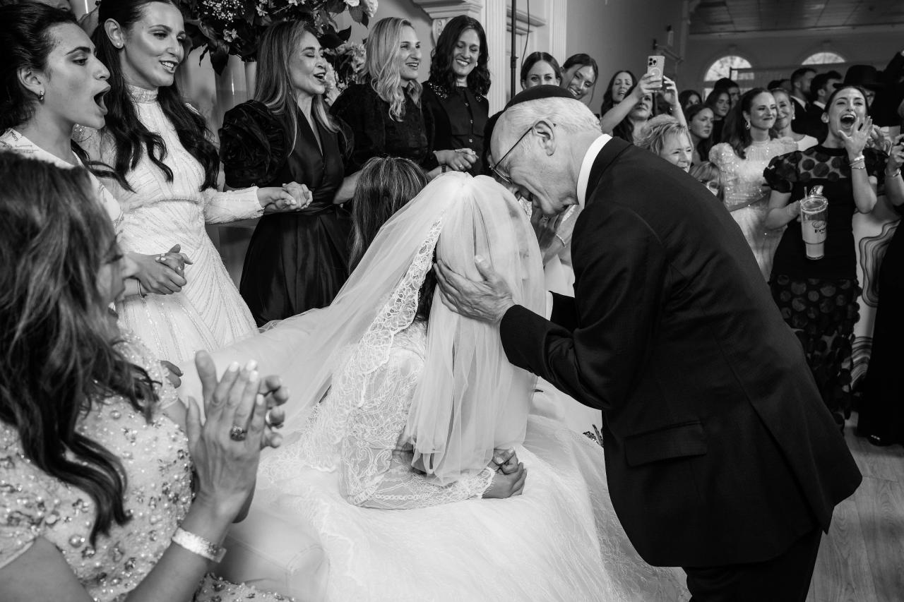 Black-and-white wedding photo of the bride embracing the groom while guests surround them, smiling and cheering during a joyful celebration. Wedding photography at Falkirk Estate Country Club, Central Valley, NY.