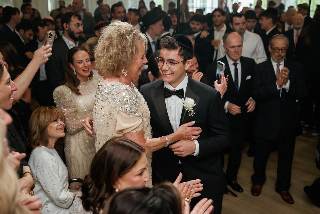 Crowded dance floor with a bride and groom embracing and laughing while guests clap and record on phones. Wedding photography at Falkirk Estate Country Club, Central Valley, NY.