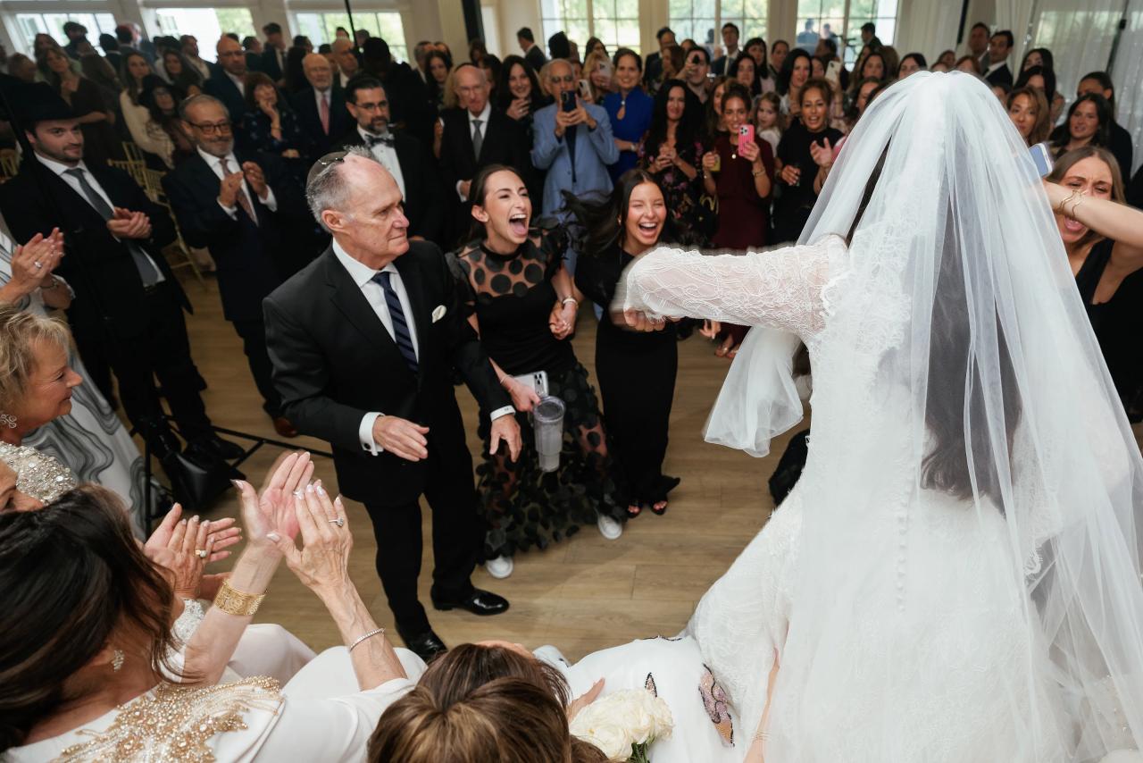 Bride in a white gown and veil dancing into a cheering crowd, with guests clapping and laughing around her. Wedding photography at Falkirk Estate Country Club, Central Valley, NY.