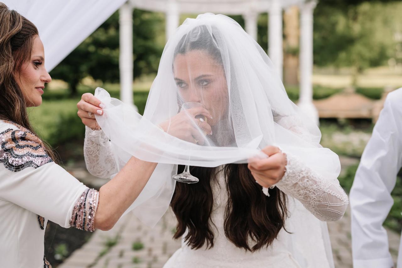 Bride during badeken as the veil is gently lifted and placed over her face outdoors in bright daylight. Wedding photography at Falkirk Estate Country Club, Central Valley, NY.