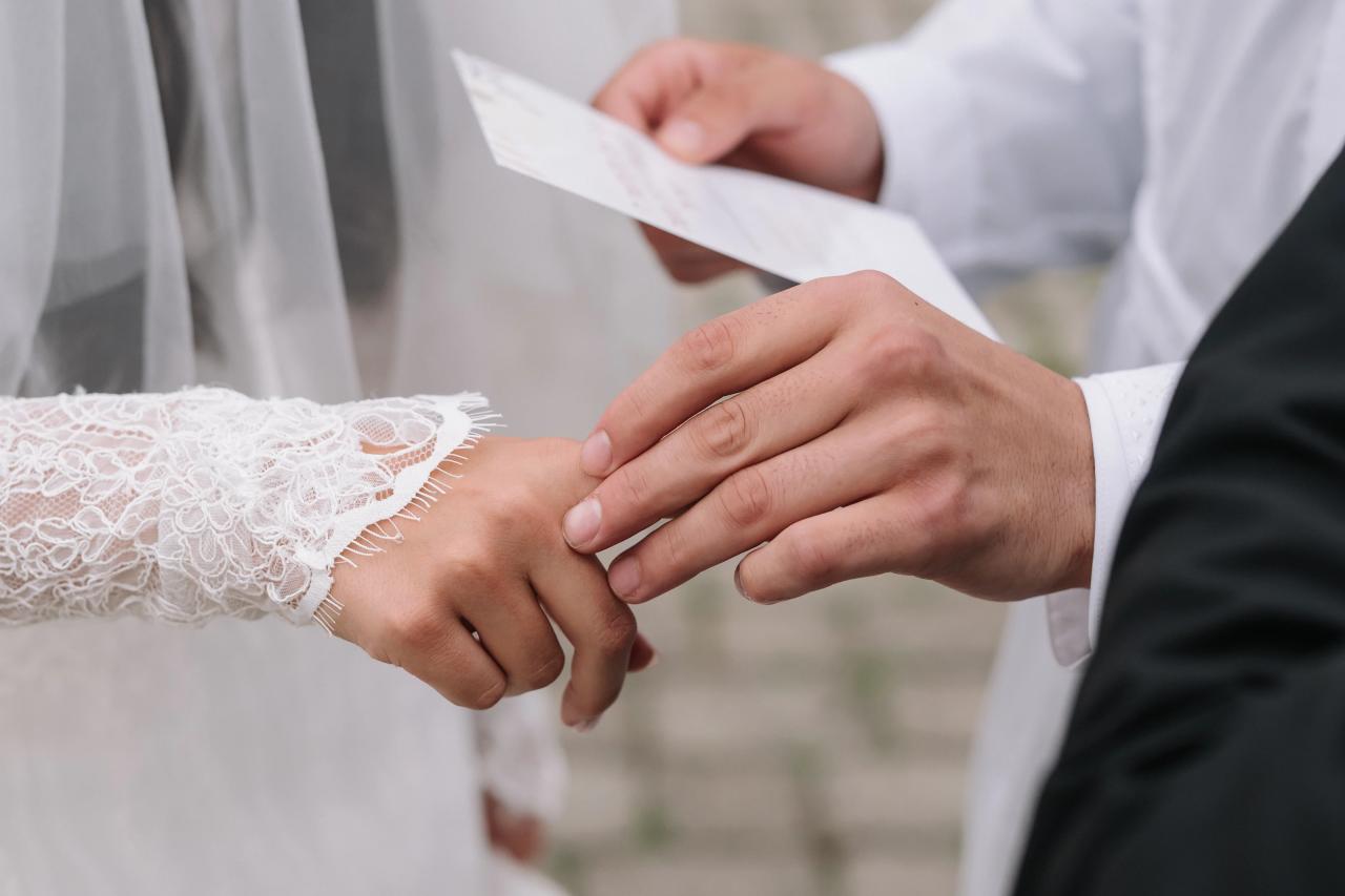 Close-up of wedding hands interlaced, with lace sleeves and a suit cuff, during the ceremony as the couple shares a quiet moment. Wedding photography at Falkirk Estate Country Club, Central Valley, NY.