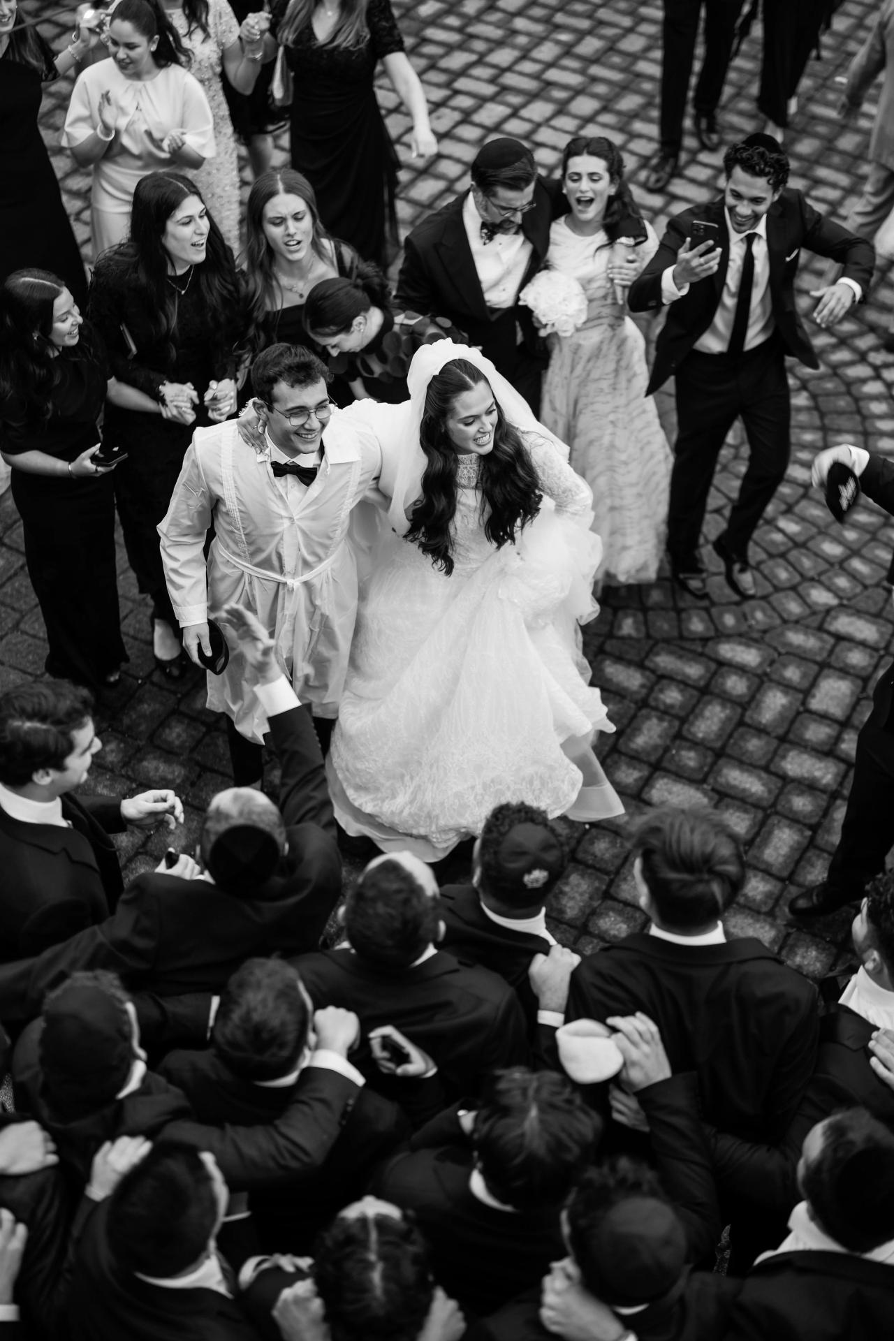 Black-and-white wedding dance-floor moment with the bride and groom moving through a ring of guests, surrounded by smiling faces and raised hands. Wedding photography at Falkirk Estate Country Club, Central Valley, NY.