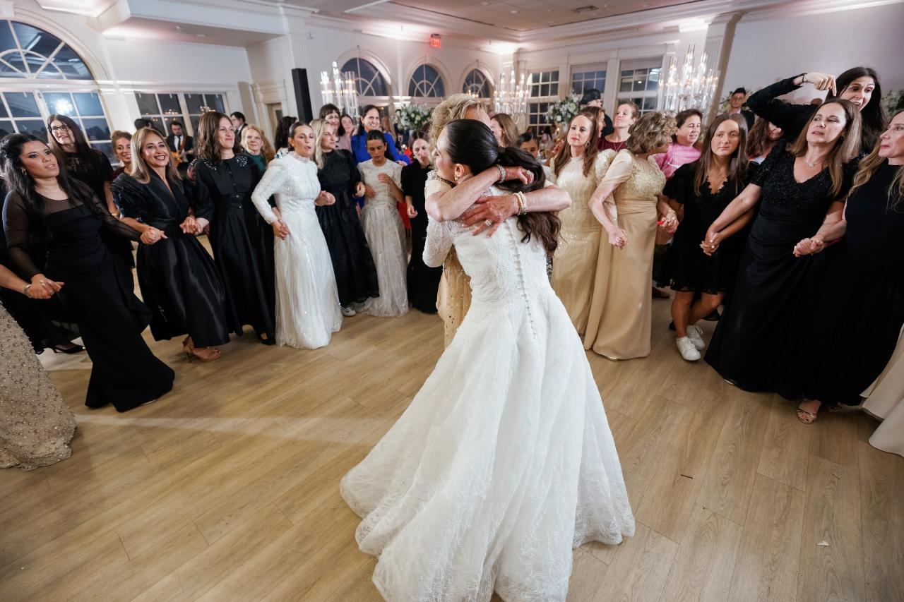Bride and groom embracing mid-dance on a ballroom floor with guests gathered around them, warm indoor lighting, joyful celebration. Wedding photography at Falkirk Estate Country Club, Central Valley, NY.