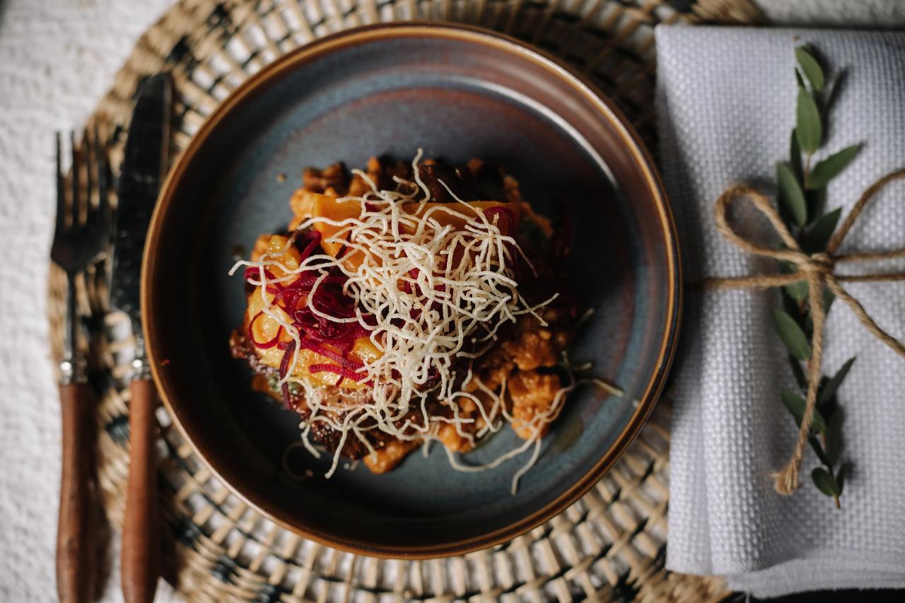 Close-up of a plated entrée with colorful sauce and fine white strands, served on a dark dish with rustic linen napkins and twine accents on the table. Bar Mitzvah photography at The Arches, Brooklyn, NY.