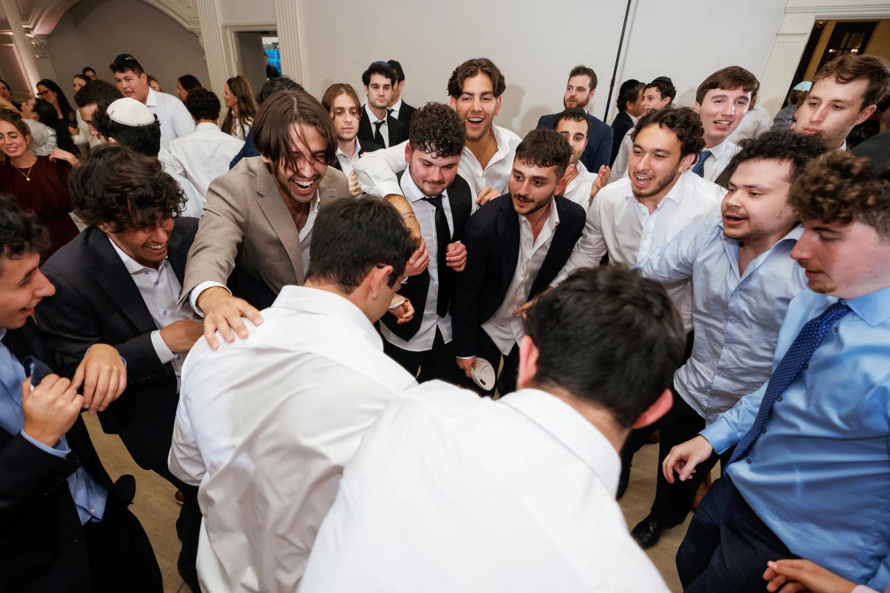 Close view of the groom laughing while surrounded by guests in a crowded dance circle at a Jewish wedding reception, with many smiling faces and a lively celebratory mood. Wedding photography at Falkirk Estate Country Club, Central Valley, NY.