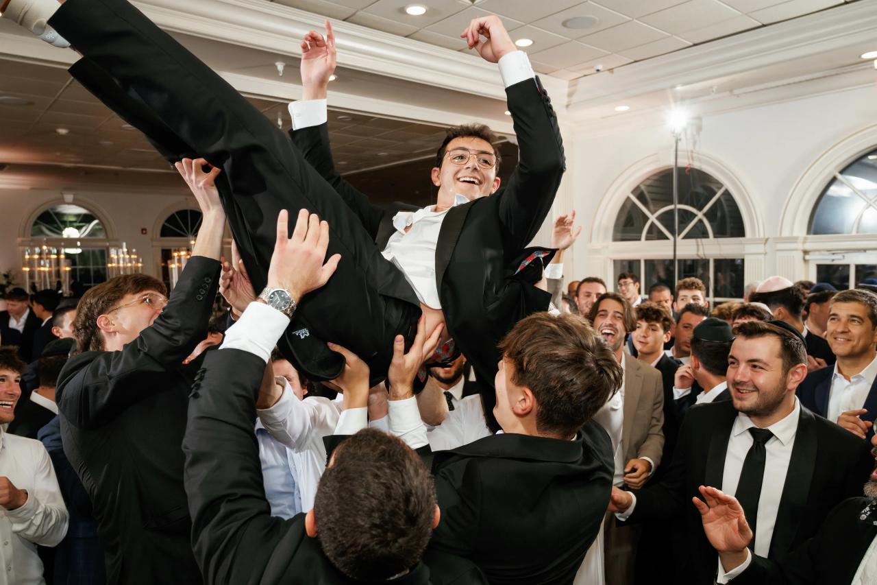 Groom laughing as guests lift him during a lively wedding celebration inside a bright ballroom. Wedding photography at Falkirk Estate Country Club, Central Valley, NY.