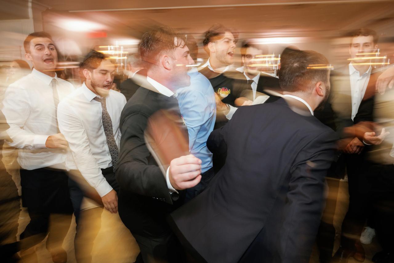 Smiling men in formalwear dancing at an event, captured with strong motion blur and warm indoor lighting. Wedding photography at Falkirk Estate Country Club, Central Valley, NY.