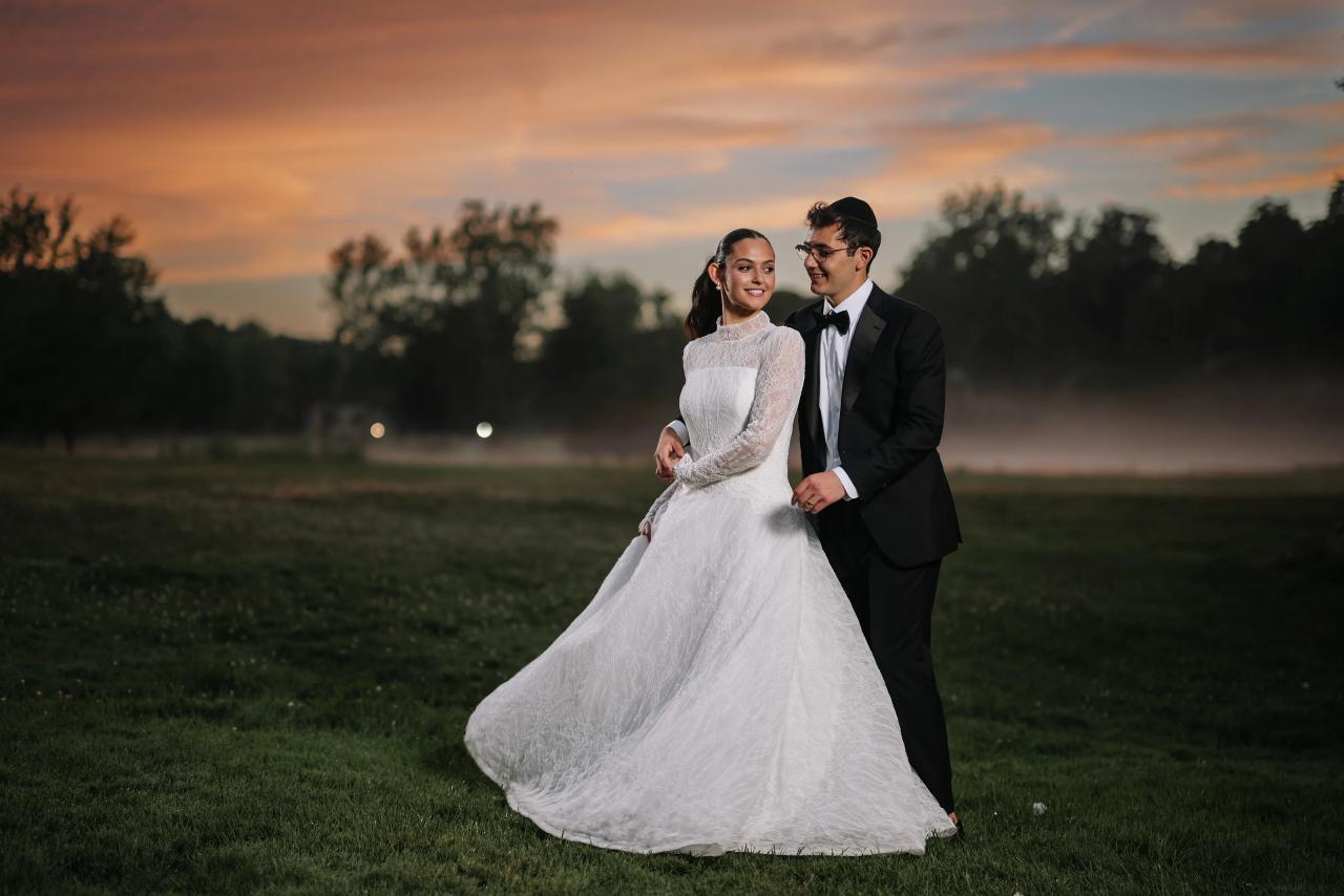 Golden-hour outdoor wedding portrait of a bride and groom walking together on a lawn at sunset, the bride’s gown flowing and both smiling. Wedding photography at Falkirk Estate Country Club, Central Valley, NY.