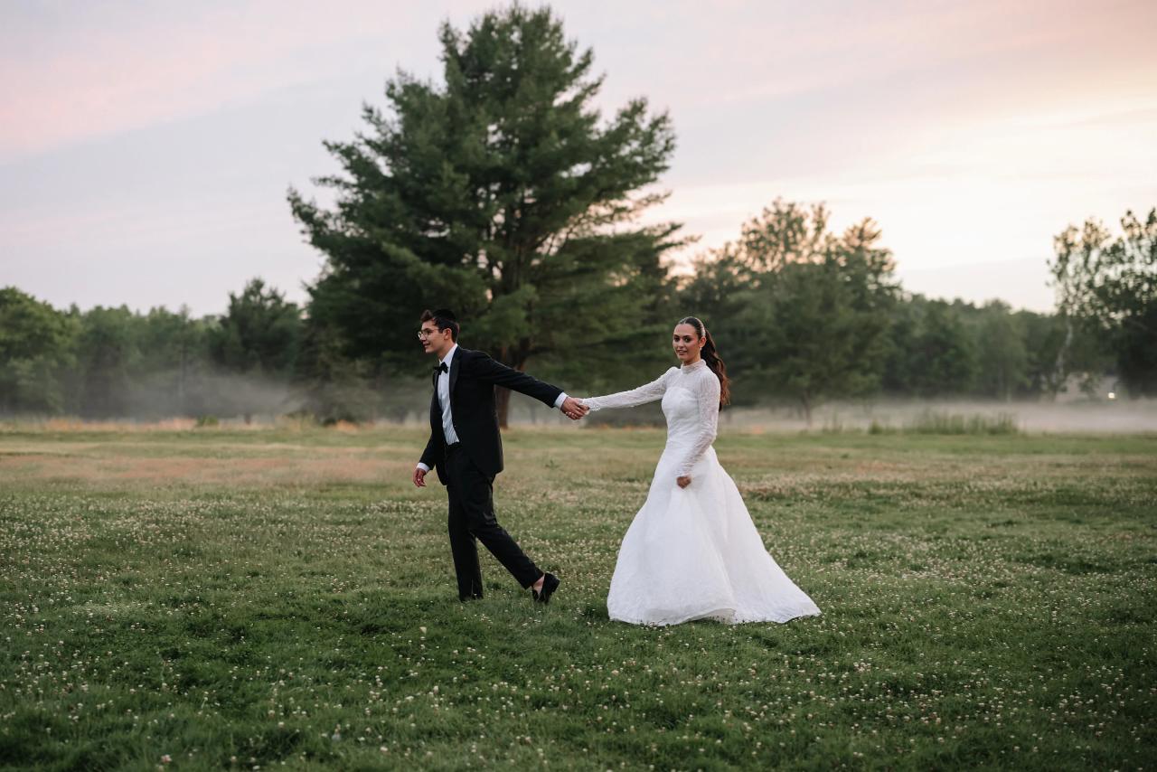 Wedding couple walking hand-in-hand across a grassy field at dusk, framed by trees and soft evening light. Wedding photography at Falkirk Estate Country Club, Central Valley, NY.