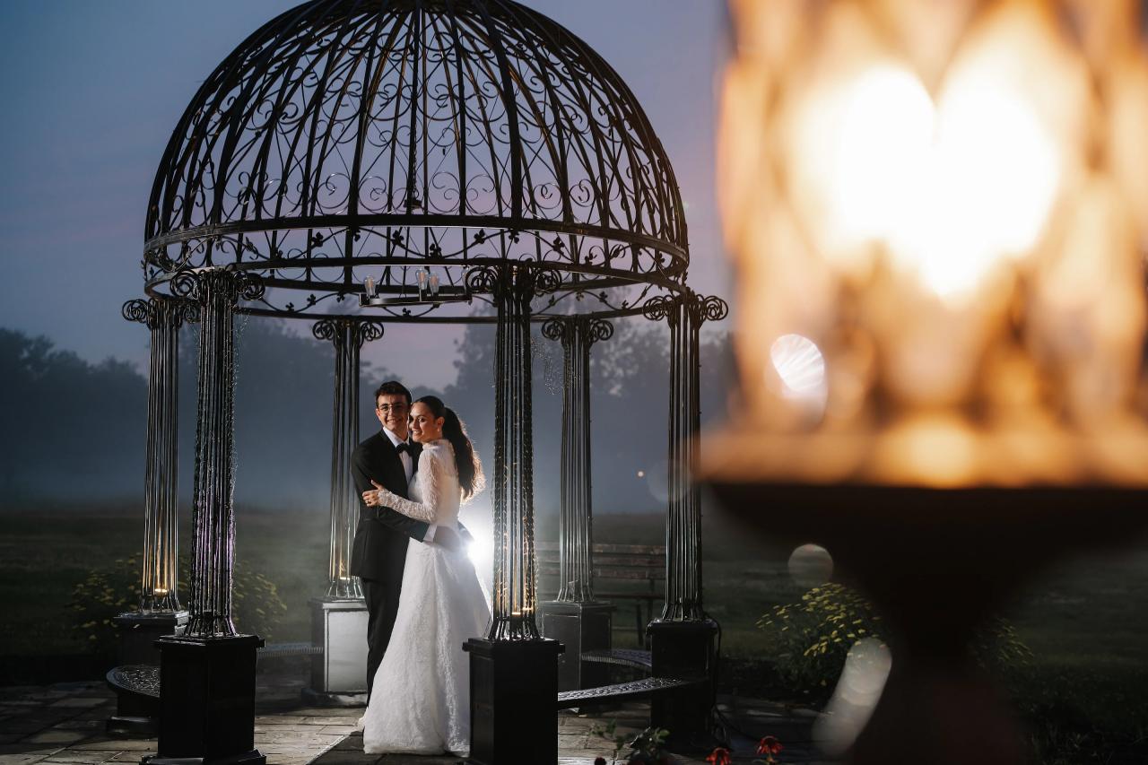 Bride and groom beneath an ornate gazebo at dusk, framed by warm candlelight in the foreground at Falkirk Estate Country Club. Wedding photography.