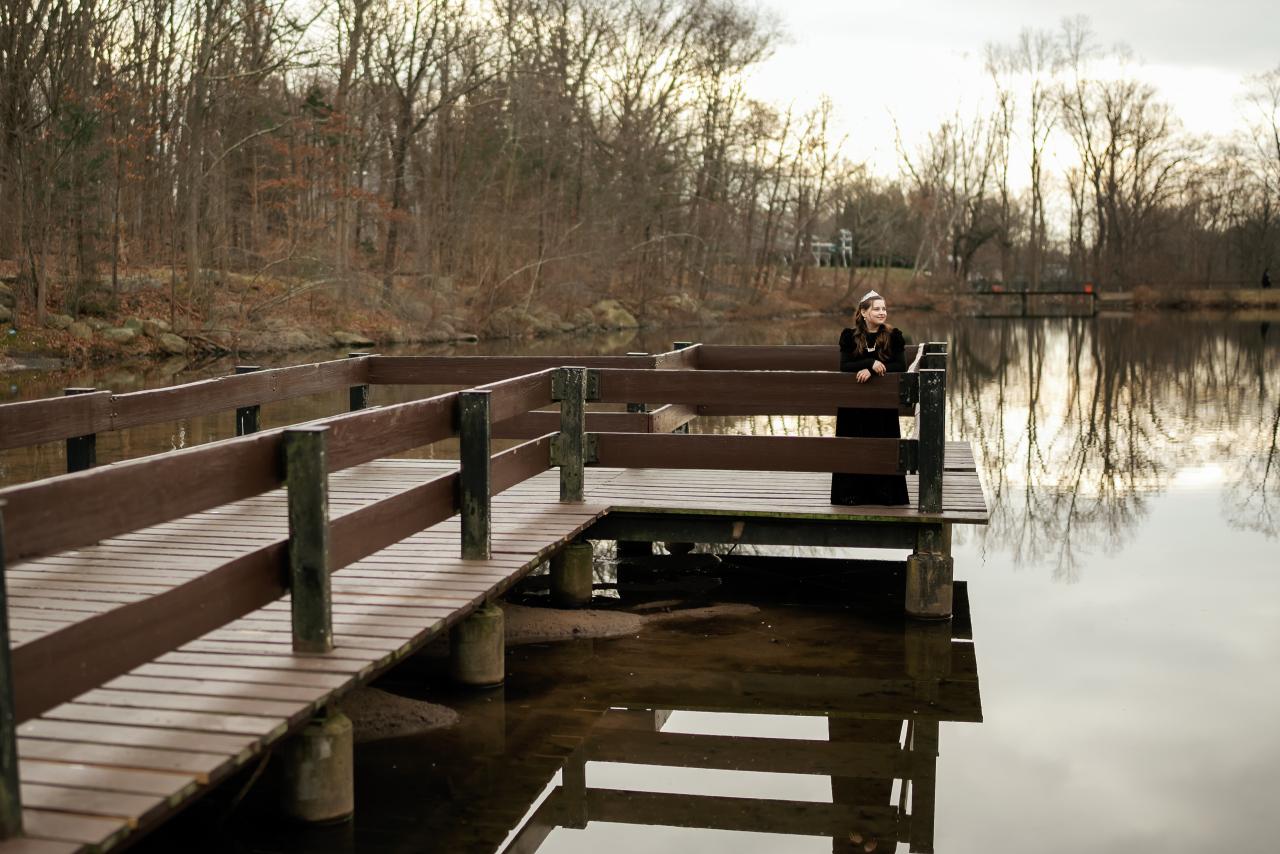 A person seated on a wooden dock by a calm lake, surrounded by leafless trees and reflected water in a quiet winter scene.