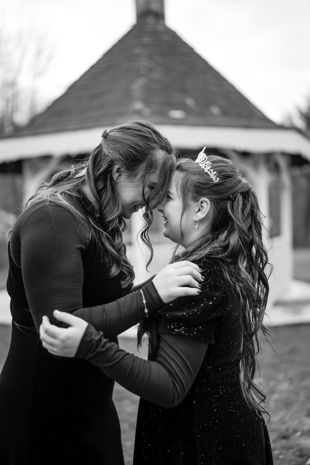 Black-and-white close-up of a mother and young girl sharing an intimate embrace under a white event canopy.