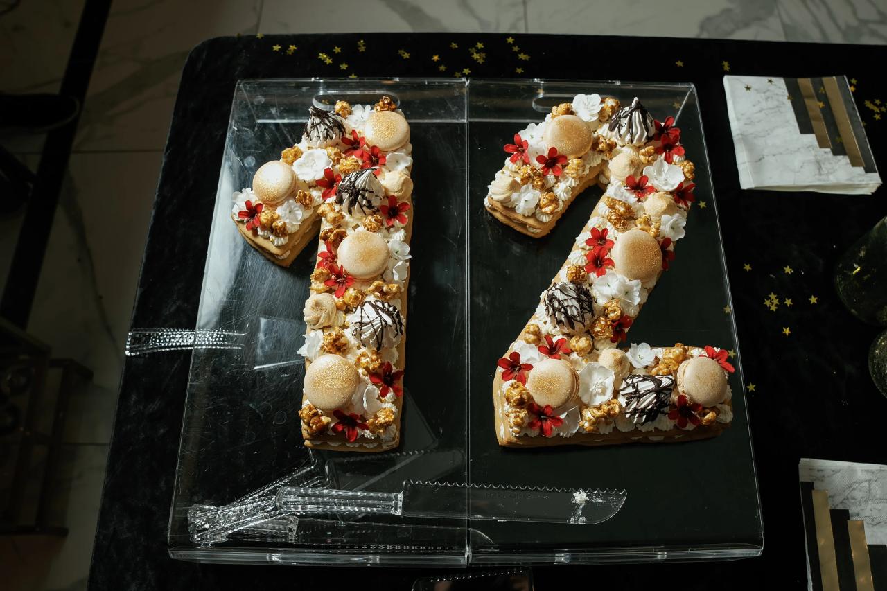 Two decorated letter-shaped cakes with gold round toppings and red-and-white floral details inside a glass display case.