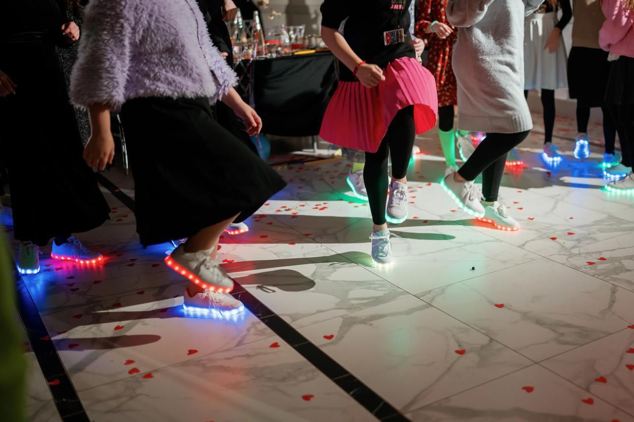 Low-angle view of guests dancing mid-step on a confetti-covered dance floor with colorful LED lights.