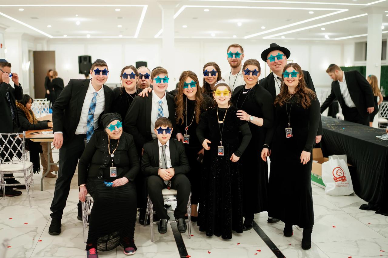 Luxury-style group portrait of guests in formal attire and matching blue sunglasses, posing together at a reception with confetti on the floor.
