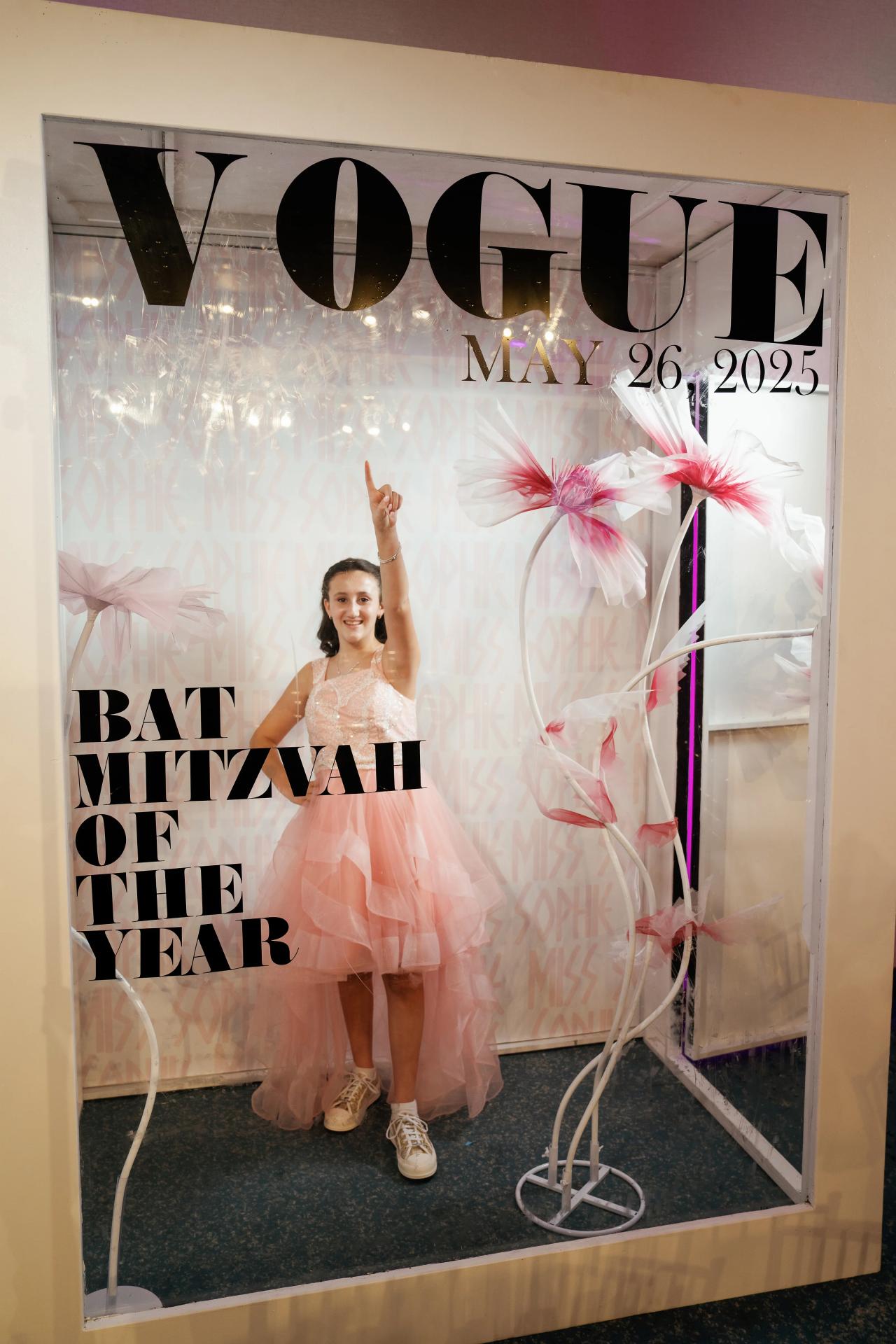 Girls standing in front of a “WOW” Bat Mitzvah photo backdrop, smiling with one arm raised, surrounded by pink decorations. Bat Mitzvah photography at Doubletree By Hilton Hotel Fort Lee - George Washington Bridge, Fort Lee, NJ.