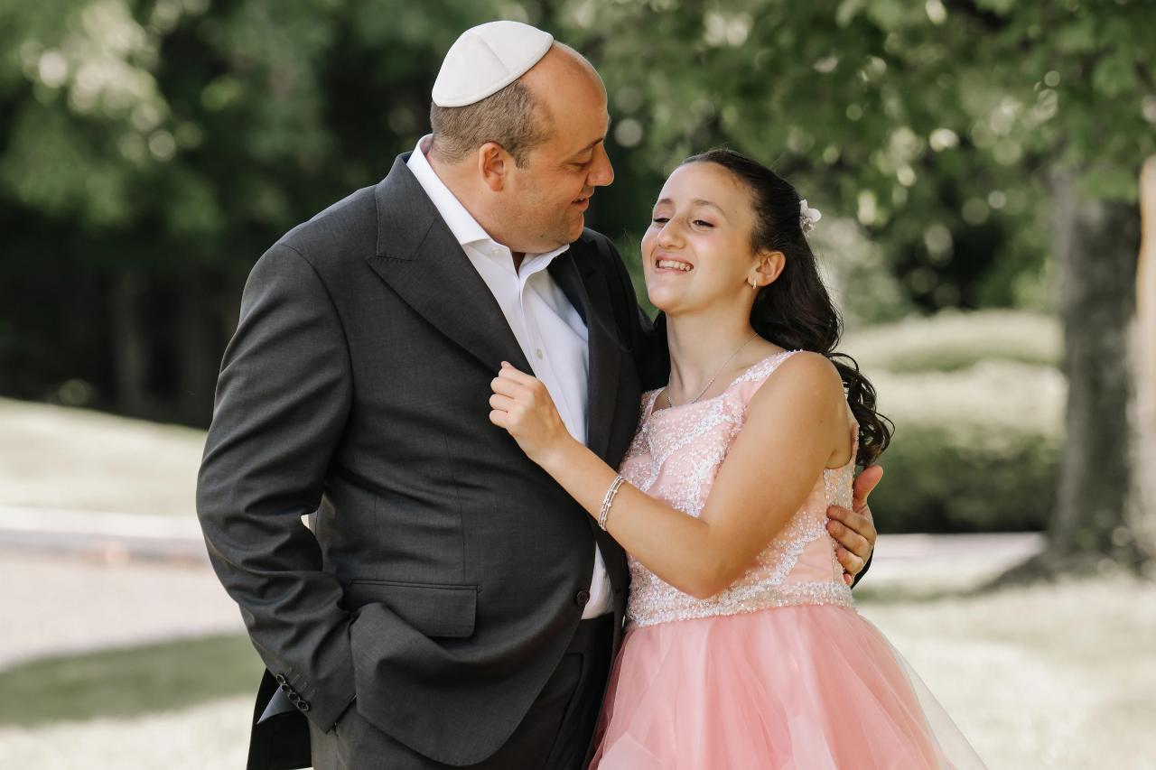 Outdoor wedding portrait of a couple in a close embrace, laughing at each other in bright daylight with a green garden background. Bat Mitzvah photography at Doubletree By Hilton Hotel Fort Lee - George Washington Bridge, Fort Lee, NJ.