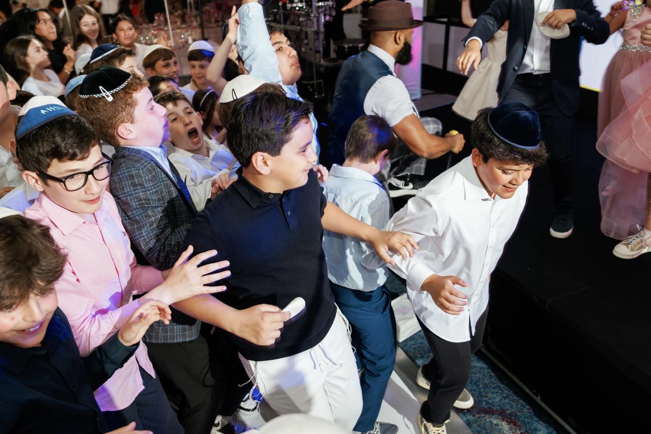 Group of young guests dancing and cheering on a wedding reception dance floor, smiling and clapping under blue party lighting. Bat Mitzvah photography at Doubletree By Hilton Hotel Fort Lee - George Washington Bridge, Fort Lee, NJ.