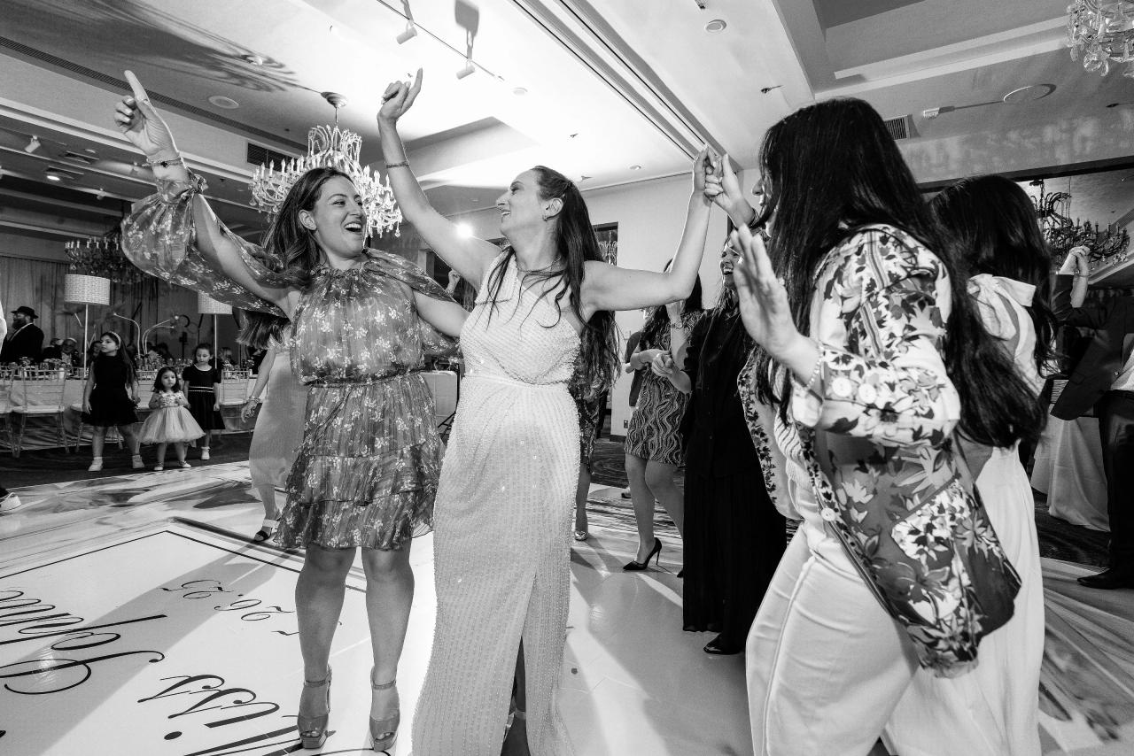 Black-and-white dance-floor moment with two guests spinning and clapping while the bride and a group celebrate, arms raised and laughing. Bat Mitzvah photography at Doubletree By Hilton Hotel Fort Lee - George Washington Bridge, Fort Lee, NJ.