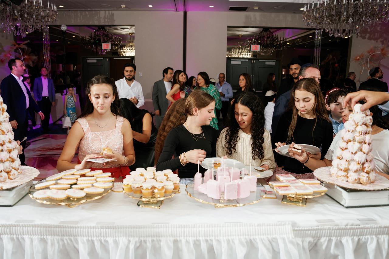 Guests seated at a reception dessert table, holding small plates while eating during a celebration. Bat Mitzvah photography at Doubletree By Hilton Hotel Fort Lee - George Washington Bridge, Fort Lee, NJ.