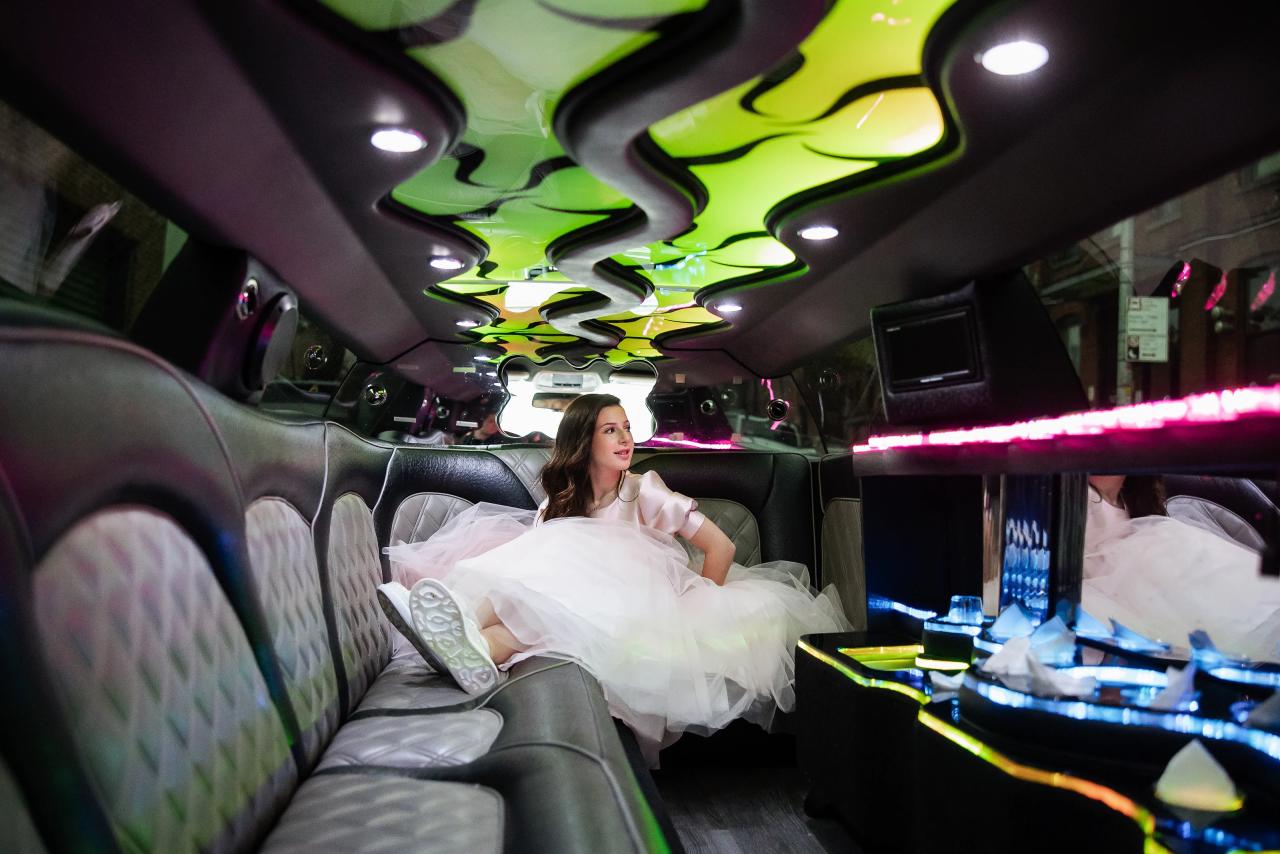 Bride reclines in a neon-lit party lounge, wearing a white tulle dress with her skirt spread, smiling as colorful lights reflect around her. Bat Mitzvah photography at Bison & Bourbon, Brooklyn, NY.