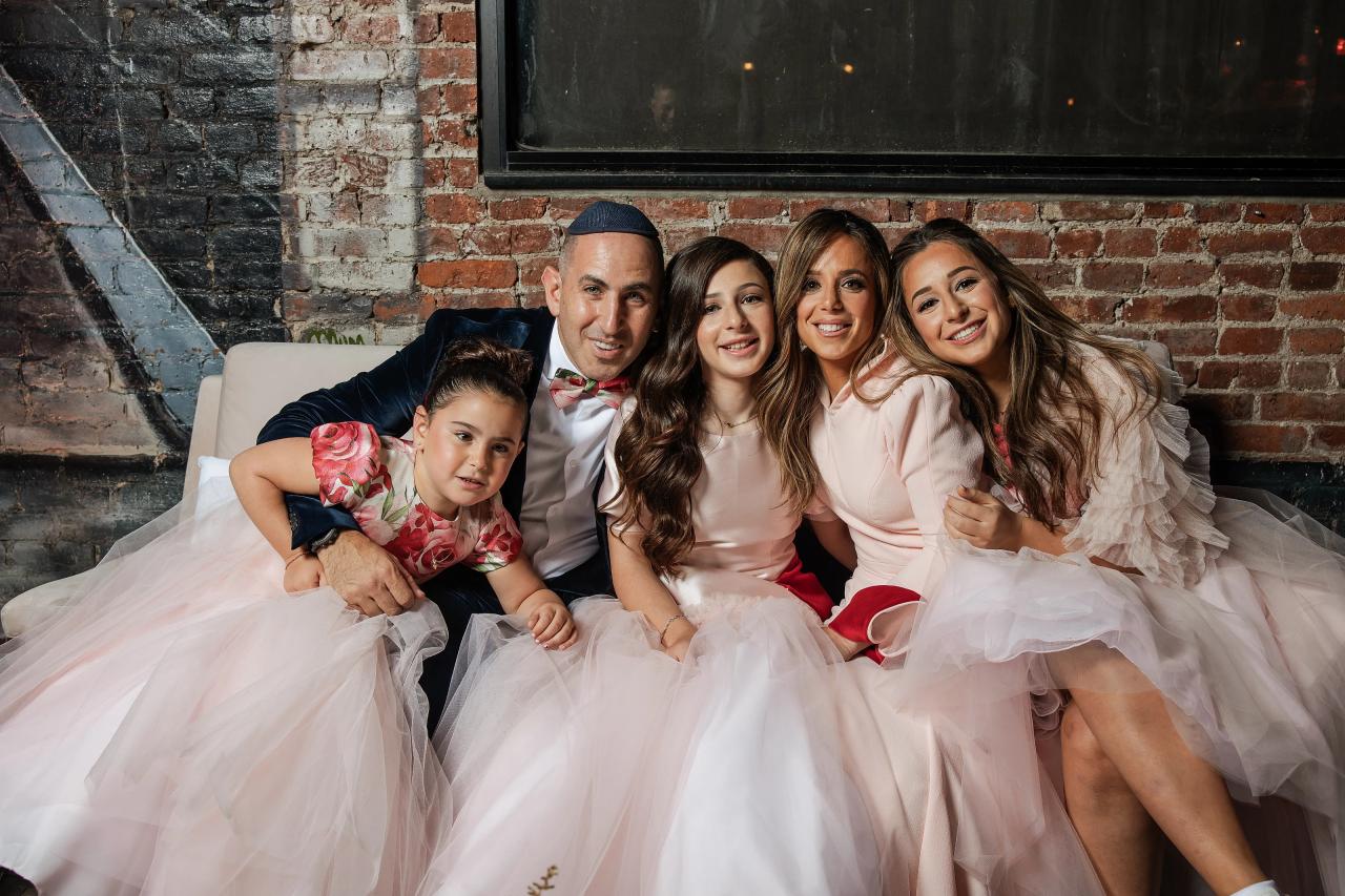 Smiling posed family group seated together at a wedding reception, wearing formal attire against a brick wall backdrop. Bat Mitzvah photography at Bison & Bourbon, Brooklyn, NY.