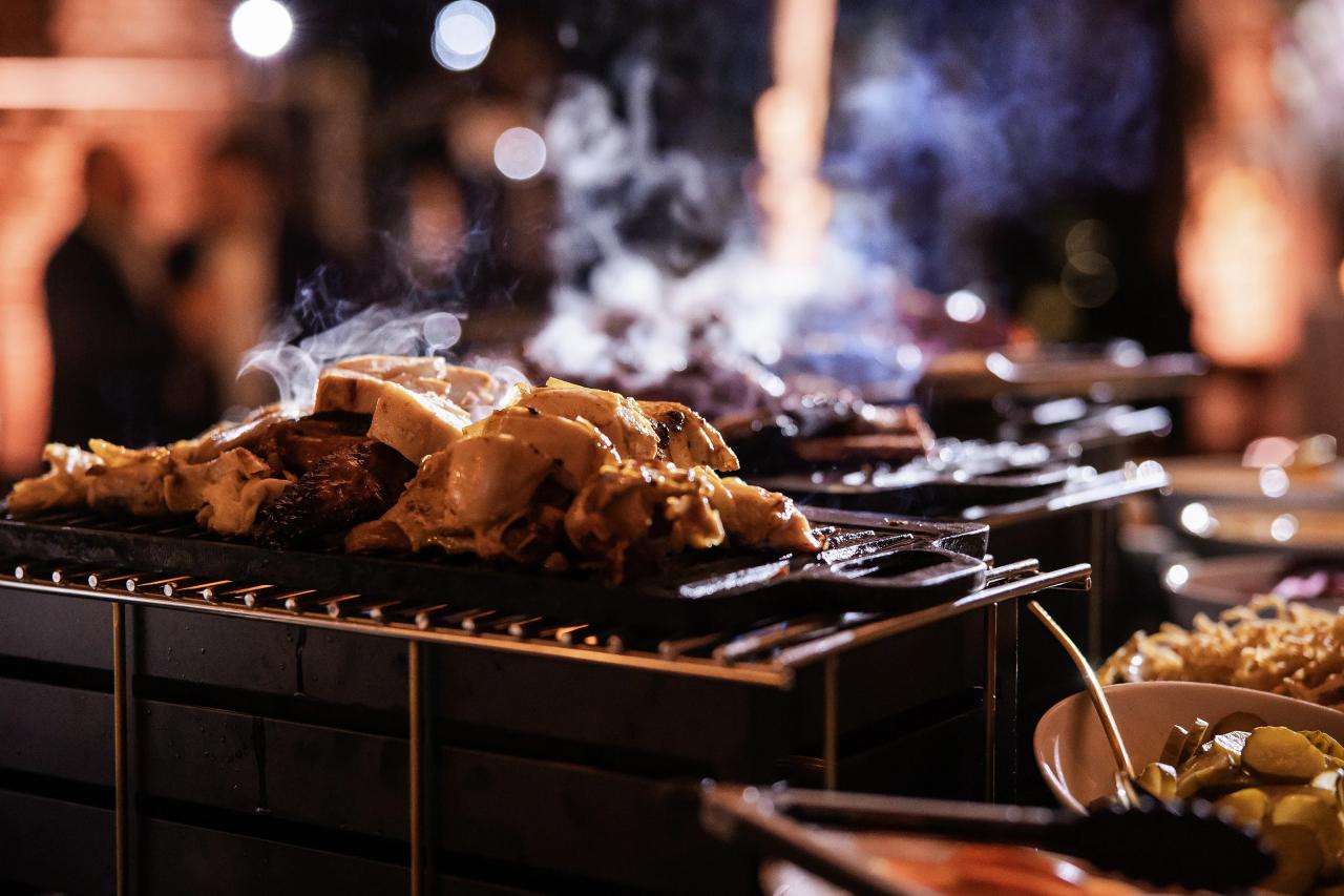 Cinematic close-up of a smoldering grill with roasted meat and smoke rising at a wedding reception. Bat Mitzvah photography at Bison & Bourbon, Brooklyn, NY.
