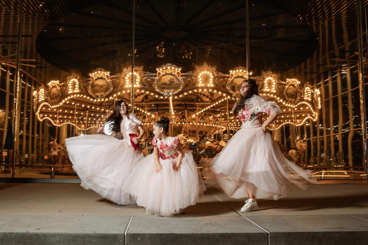 Two children in white flower girl dresses twirl and run in front of an illuminated ornate carousel backdrop at a reception. Bat Mitzvah photography at Bison & Bourbon, Brooklyn, NY.